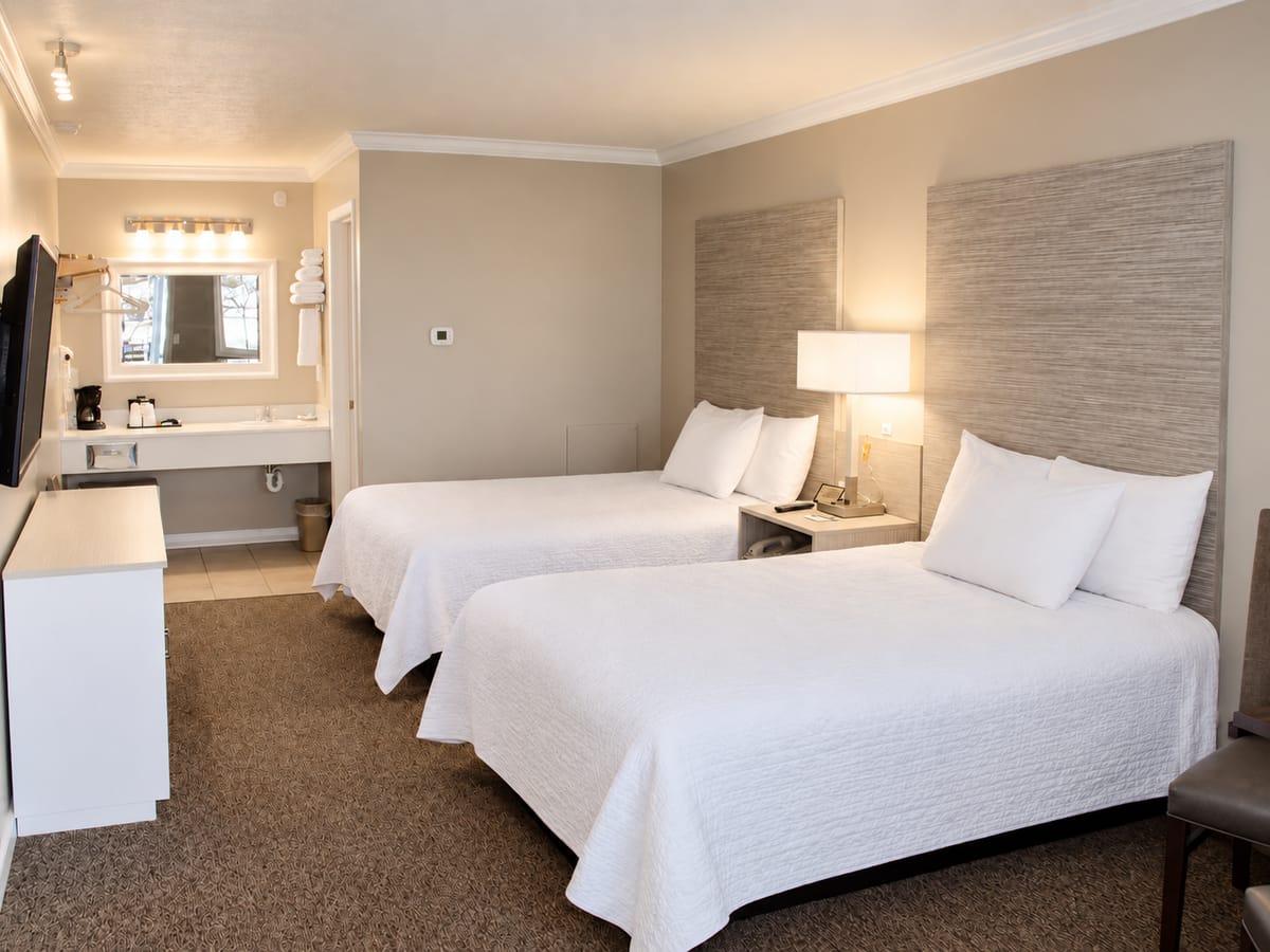 Two double beds with white bedding and a vanity in a Berlin Village Inn room